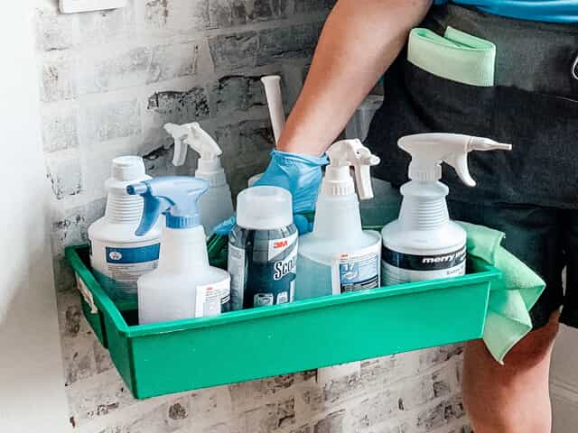 Merry Maids cleaning professional holding a tray of cleaning supplies and green cleaning products