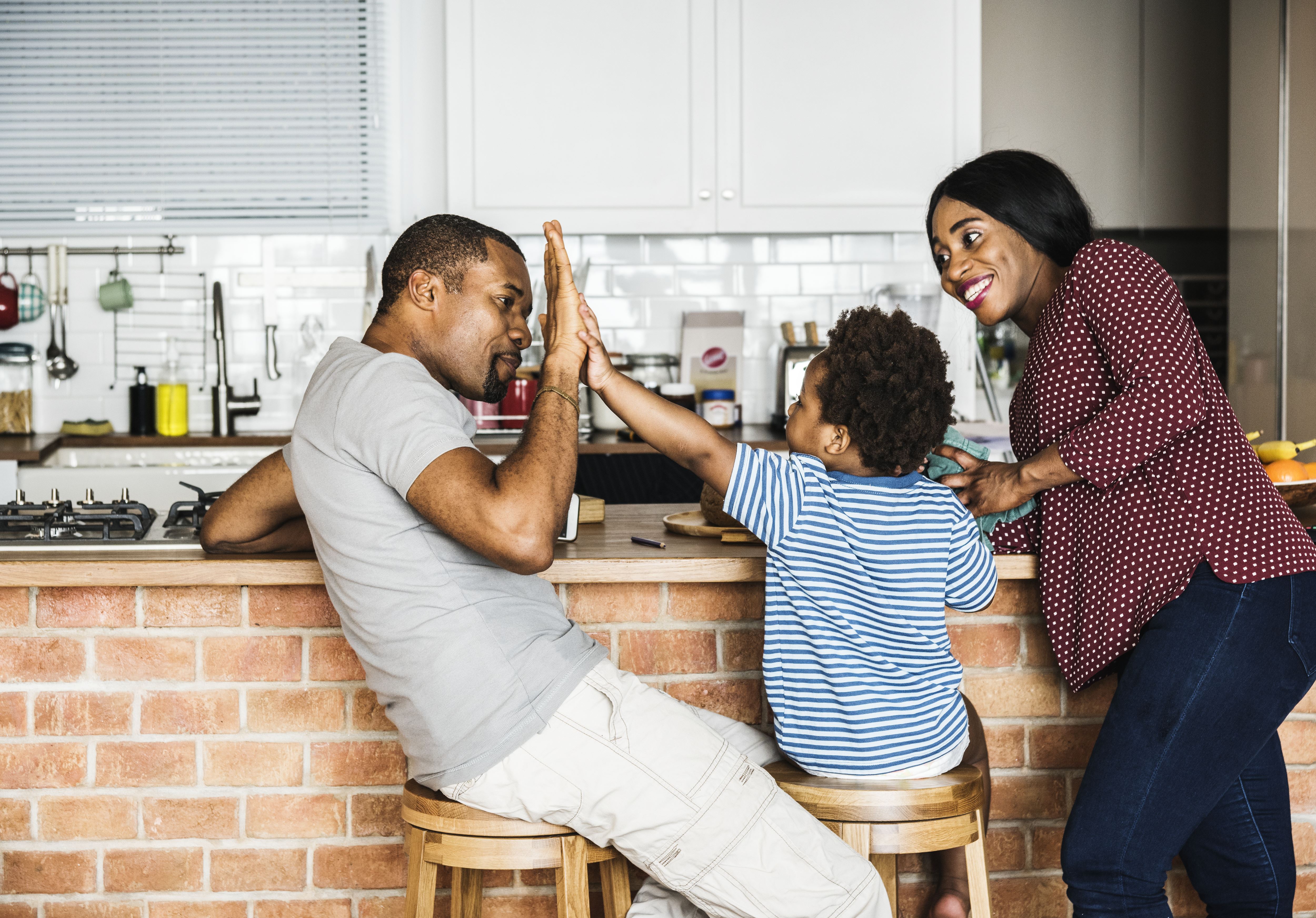 In a kitchen recently cleaned during maid service from Merry Maids of Virginia Beach, a father and son high-five while a mother watches them happily