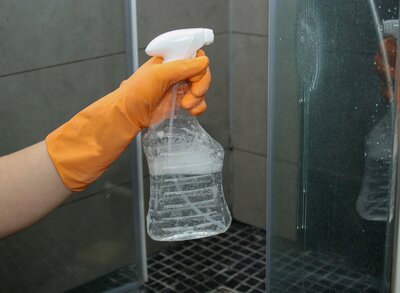 A person spraying a cleaner on glass shower doors