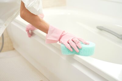 A person using a sponge to clean a fiberglass bathtub