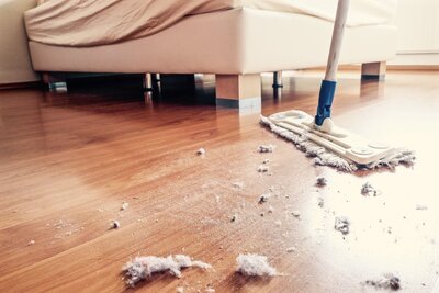 A hardwood floor duster being used to collect dust from under a bed