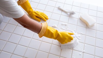 A person using a scrub brush to clean a tile shower floor