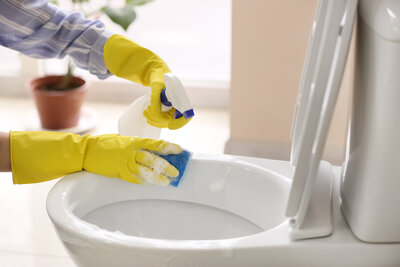 A woman wearing yellow gloves cleaning a toilet