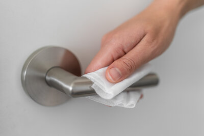 A person using a wipe to disinfect a door handle