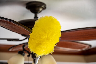 A yellow dust wand being used to dust a ceiling fan