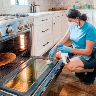 Professional providing house cleaning services by scrubbing oven door